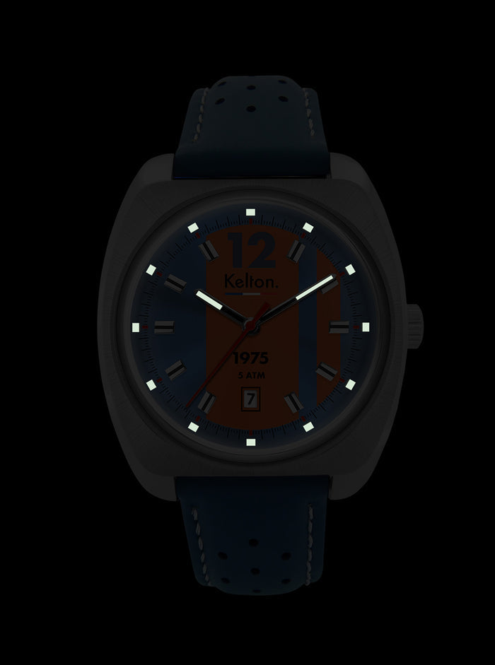 Montre Kelton sur fond sombre, cadran bleu-orangé, boîtier argenté et bracelet cuir bleu.